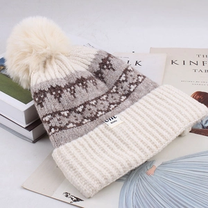 Detailed knit texture of the beige beanie with a large fluffy pom-pom and brand label