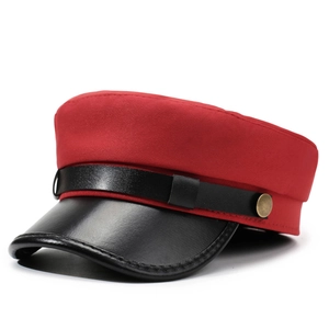 Détail d'une casquette militaire rouge avec visière en cuir noir et bouton en bronze