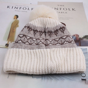 Detail of winter knit beanie with geometric patterns and a large fluffy faux fur pompom