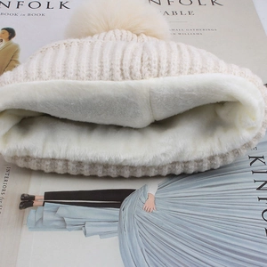Detail view of beige knitted hat showing thick white plush fleece lining and fur pompom