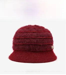 Dettaglio del cappello a secchiello in maglia bordeaux con texture morbida e fiocco d'oro