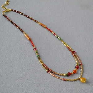 Close-up of bohemian layered beaded necklace with orange stones and gold lobster clasp