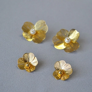 Detailed macro view of woven gold wire flower earrings with pearls and metallic beads