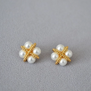 Détail de boucles d'oreilles en métal doré torsadé avec quatre perles blanches en croix
