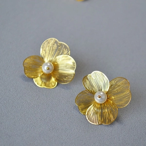 Close-up of golden hollow flower earrings with textured petals and centered pearls