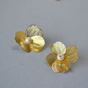 Detailed close-up of golden hollow mesh flower earrings with central white pearl accents