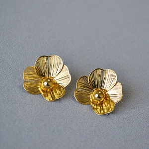 Close-up of golden hollow double-layer flower earrings with textured petals and center bead