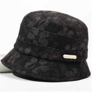 Close-up of black floral fabric texture and golden metal logo on the baker boy hat
