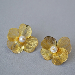 Detail of woven gold flower stud earrings featuring a central white pearl inlay