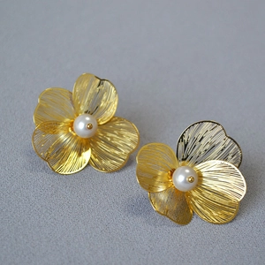Macro detail of gold-plated layered flower earrings with intricate filigree and pearls