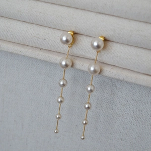 Macro detail of long drop pearl earrings with gold chain on natural linen fabric
