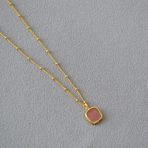 Detail of square reddish-brown stone pendant on a gold beaded chain necklace