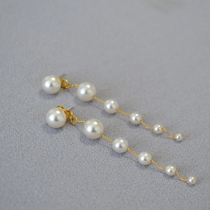 Detail of long drop earrings featuring gradient white pearls on elegant gold tassels