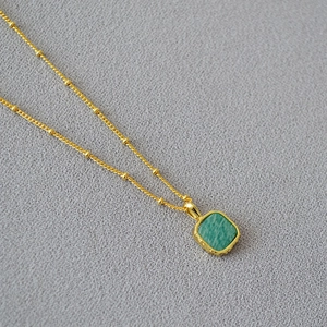 Macro detail of geometric square green stone pendant on golden beaded chain necklace