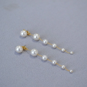 Detail of long gradient pearl tassel earrings with thin gold chains on textured cloth
