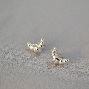 Macro view of silver croissant earrings with spiral texture on a grey fabric base