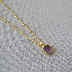 Detail of gold beaded satellite chain with a square purple semi-precious stone pendant