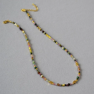 Colorful tourmaline heart beaded necklace with gold accents on a textured grey background