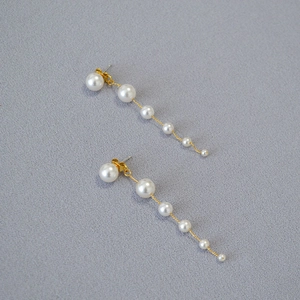 Detailed close-up of gold chain earrings with elegant gradient white pearls on grey fabric