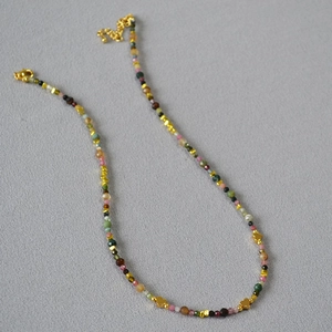 Colorful tourmaline beaded necklace with golden heart charms on grey fabric background