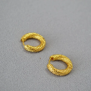 Detailed view of golden twisted rope texture on circular hoop earrings with metallic finish