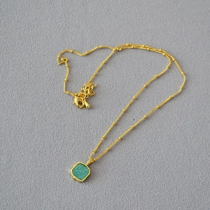 Detail of satellite chain necklace featuring a square green gemstone and lobster clasp