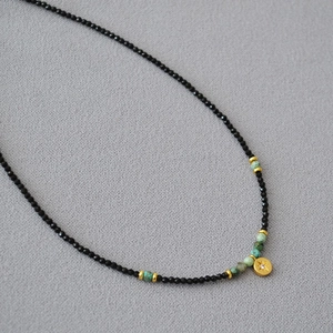 Macro shot of black spinel beads with turquoise accents and a golden star pendant