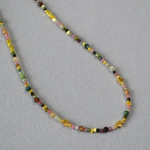 Detail of colorful faceted tourmaline beaded necklace with gold heart charms on gray fabric