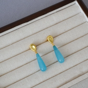 Detail of teardrop blue stone earrings in gold matte finish on a jewelry box display
