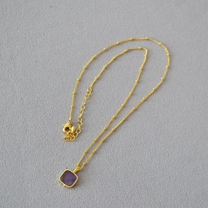 Detail of gold satellite chain necklace with a square purple faceted stone pendant