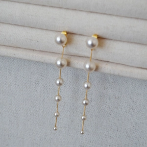 Detailed view of long tassel earrings with gradient sized white pearls on gold chains