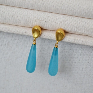 Detail of matte gold studs with translucent light blue teardrop stone pendants on fabric