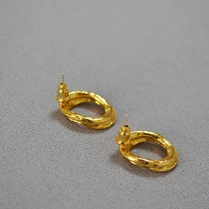 Close-up of golden earrings with irregular lava texture and hammered metal surface