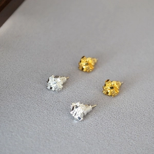Macro view of irregular gold and silver brass stud earrings on grey fabric background