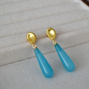Minimalist gold brass earrings with blue teardrop pendants on linen jewelry display tray