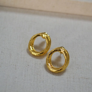 Irregular textured gold plated oval stud earrings on grey linen fabric background
