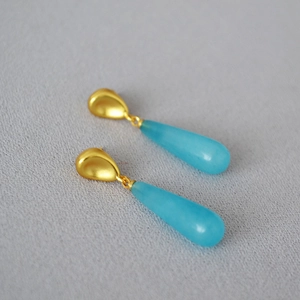 Detailed macro of gold drop earrings with teardrop blue chalcedony stones and matte finish