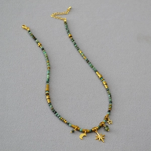 Detail of turquoise beaded necklace featuring gold moon and star charms on textured fabric