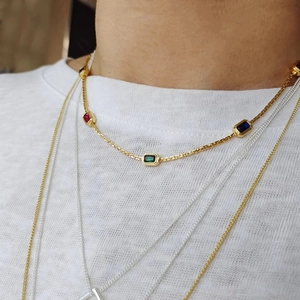 Close-up of layered gold chain necklace with emerald-cut red, green and blue gemstones