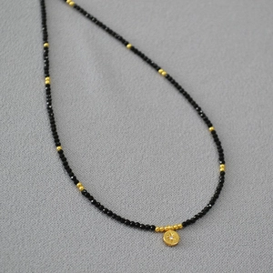 Detail of beaded necklace featuring black spinel beads and a golden star engraved pendant