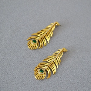 Detailed close-up of peacock feather earrings with green gemstone and gold plating