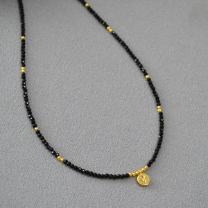 Detail of beaded necklace with faceted black stones and golden starburst pendant