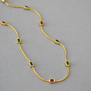 Detailed view of gold necklace with rectangular red green and blue gemstones on grey surface