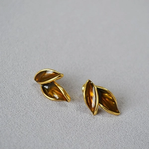 Vintage gold-edged amber leaf stud earrings on a textured light grey fabric background