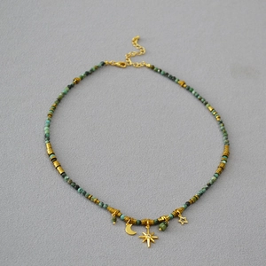 Close-up of turquoise beaded necklace with gold moon and star pendants on grey background