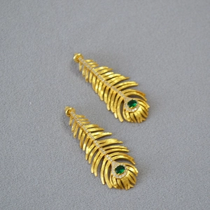 Macro shot of gold feather earrings with emerald green stone and sparkling zircon details