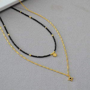 Detail of double-layered necklace featuring black beads and golden star charms on grey fabric