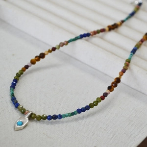 Détail macro d'un collier de perles colorées avec un pendentif flèche argentée et turquoise