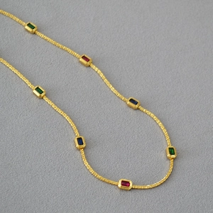 Detail of gold chain necklace featuring red, blue and green rectangular gemstones