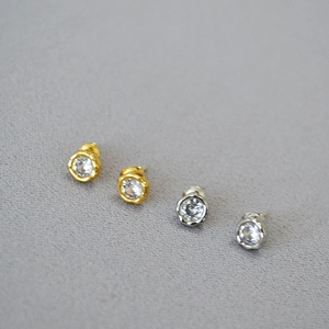 Macro view of minimalist irregular bezel-set zircon stud earrings in gold and silver